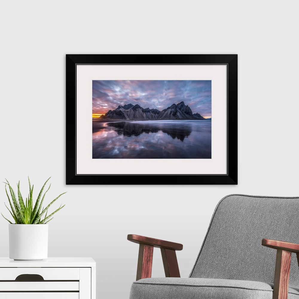 A modern room featuring Rugged mountain peaks and a colourful sunset reflected in tranquil water. Iceland.