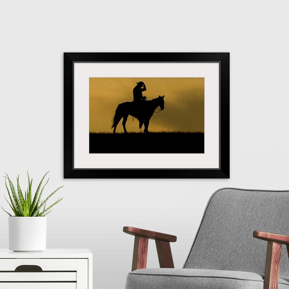 A modern room featuring Silhouette of a cowboy on a horse against a sky of golden cloud at sunset; Montana, United States...