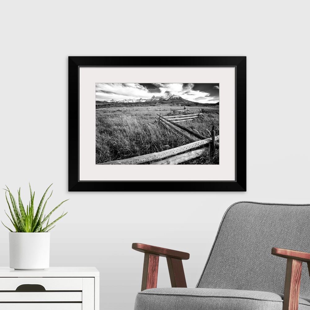 A modern room featuring Black and white landscape photograph of a field with tall grass and a wooden fence creating leadi...