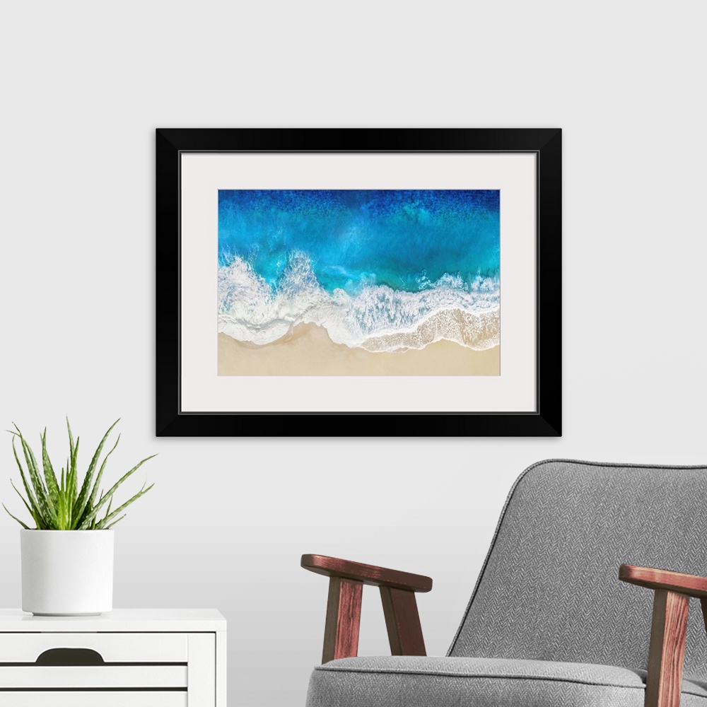 A modern room featuring One artwork in a series of aerial shots of a beach as blue waves break upon the shore.