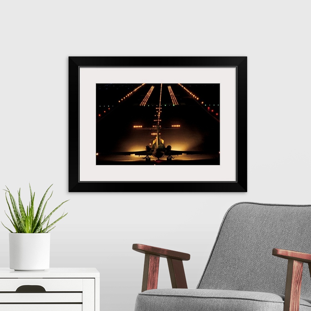 A modern room featuring Giant photograph shows a small aircraft stationed at the end of a brightly lit airstrip at nightt...