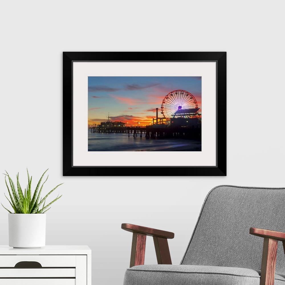 A modern room featuring Large artwork of a beach pier during sunset skies with the rides lit up and ocean waves calmly cr...