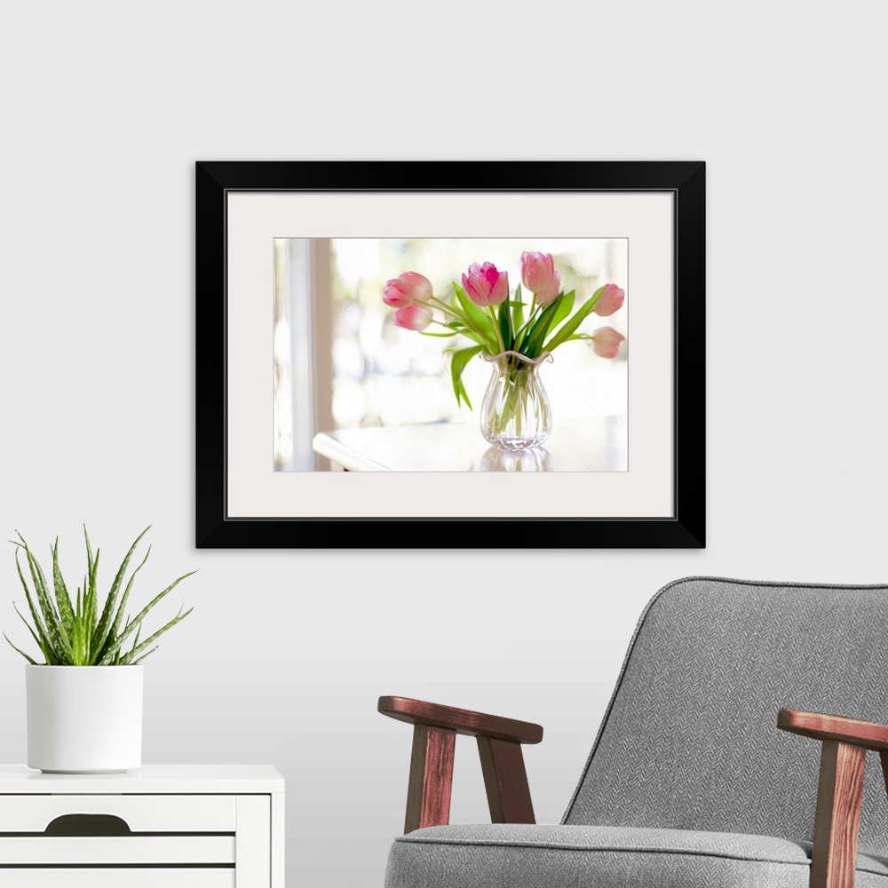 A modern room featuring Ruffled pink glass vase filled with soft, pink tulips sitting on table in front of window bright ...