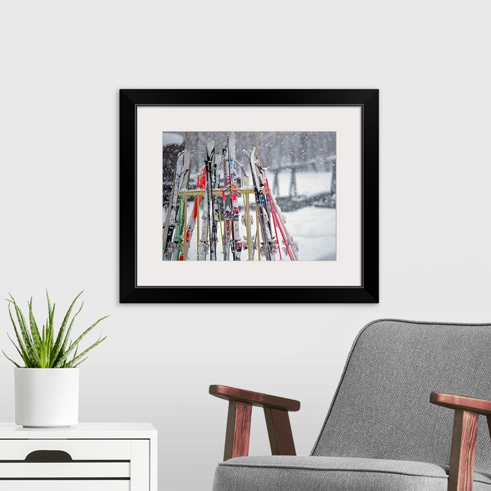 A modern room featuring In this photograph multiple skis are stored on an outside rack as large white snowflakes fall all...