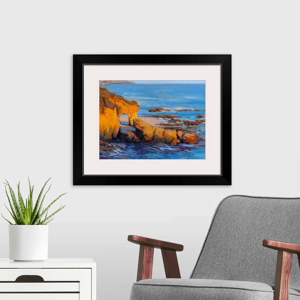 A modern room featuring Horizontal contemporary painting of a rocky cliff and a beach with vivid blue water.