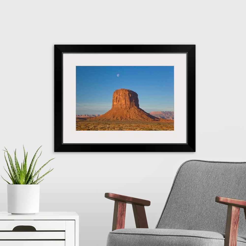 A modern room featuring Moon visible over rock formation in Monument Valley in early morning.