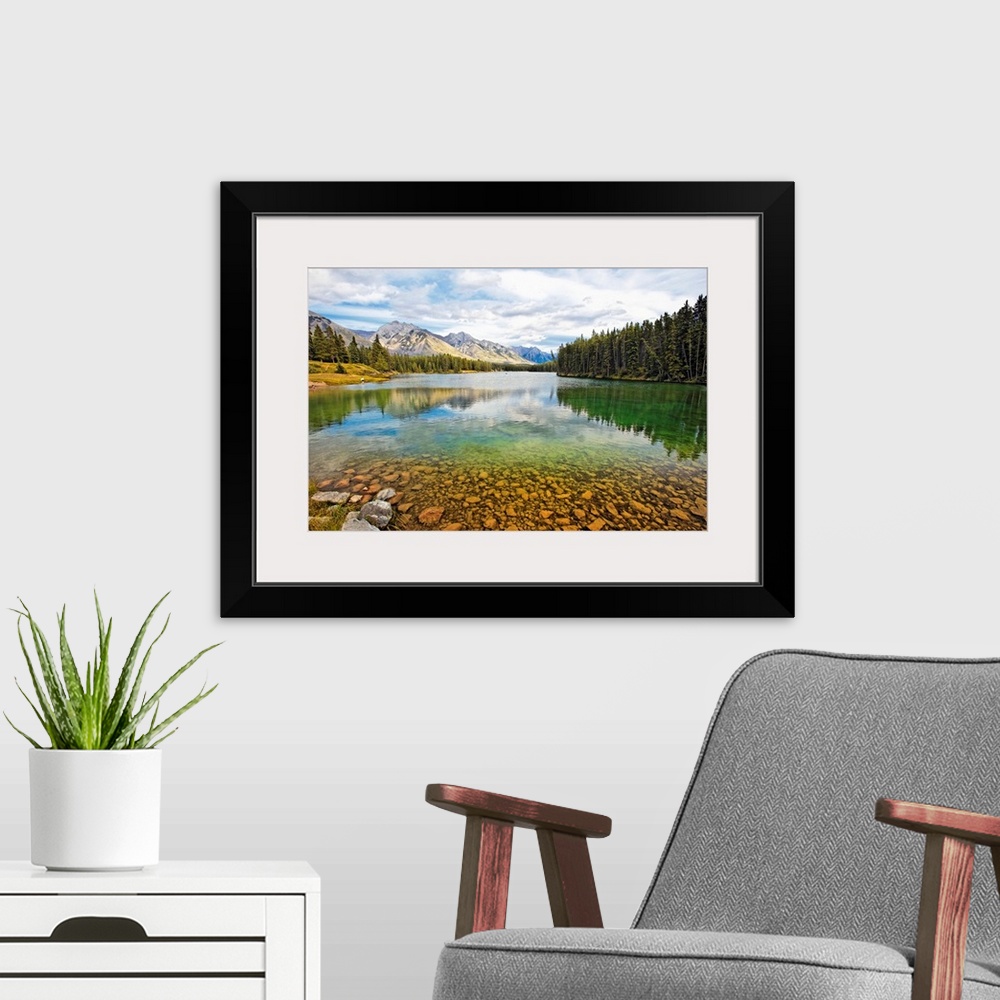 A modern room featuring Giant photograph taken from the rocky shores of a lake that is surrounded by dense forests and sn...