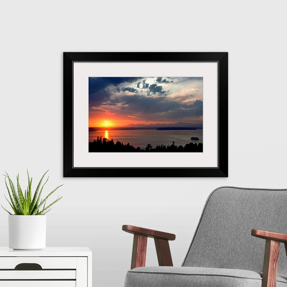 A modern room featuring Horizontal photograph of a vibrant setting sun in a partly cloudy sky, over a large body of water...