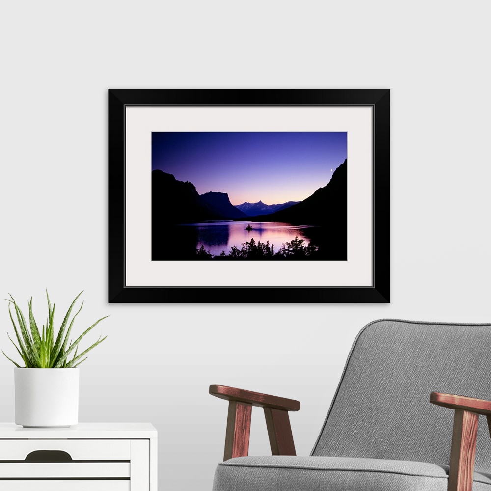 A modern room featuring Mountainous terrain is silhouetted by the sunset and a large body of water sits in between. A sma...