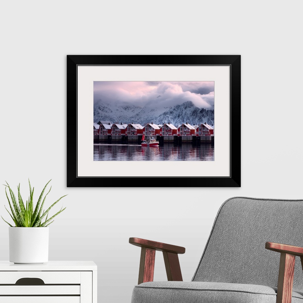 A modern room featuring A photograph of a red building sitting on the shoreline of a snowy landscape with mountains in th...