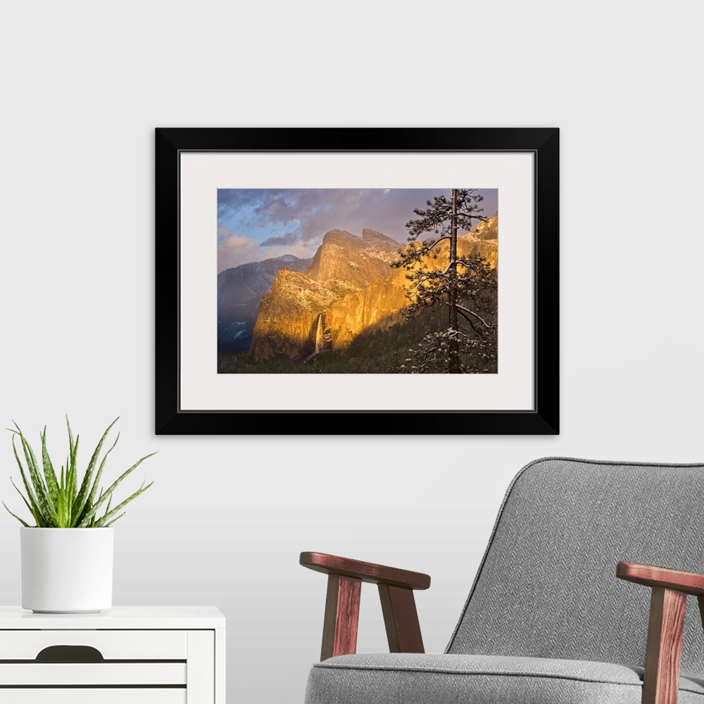 A modern room featuring Large canvas photo print of big rugged mountains with a waterfall highlighted with the warm color...