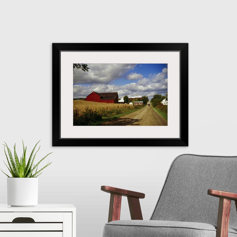 A modern room featuring Photograph of wheat field, barn and farmhouses along dirt road under a cloudy sky.