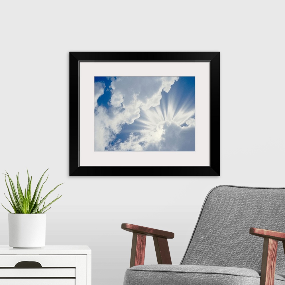 A modern room featuring Large photograph of the sky on a cloudy day with the sun's rays about to break through.