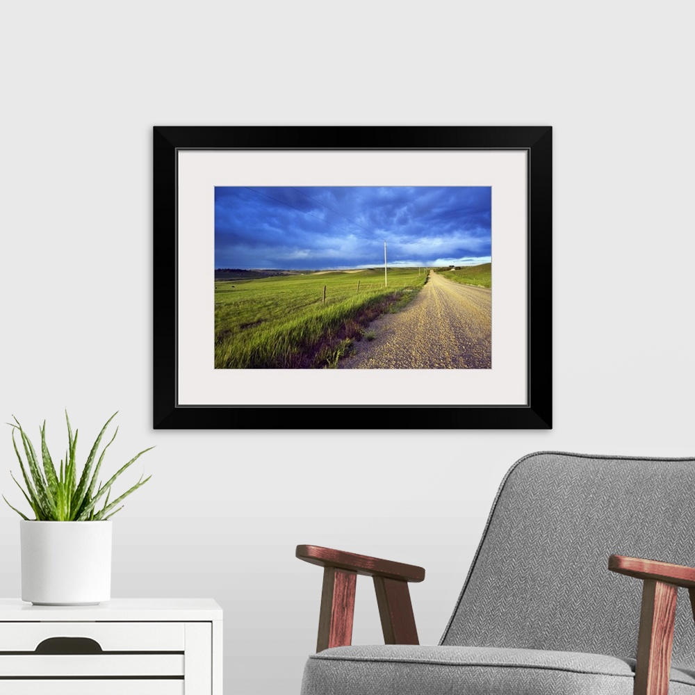 A modern room featuring Landscape, oversized photograph of a gravel road, open fields on wither side, beneath a stormy sk...