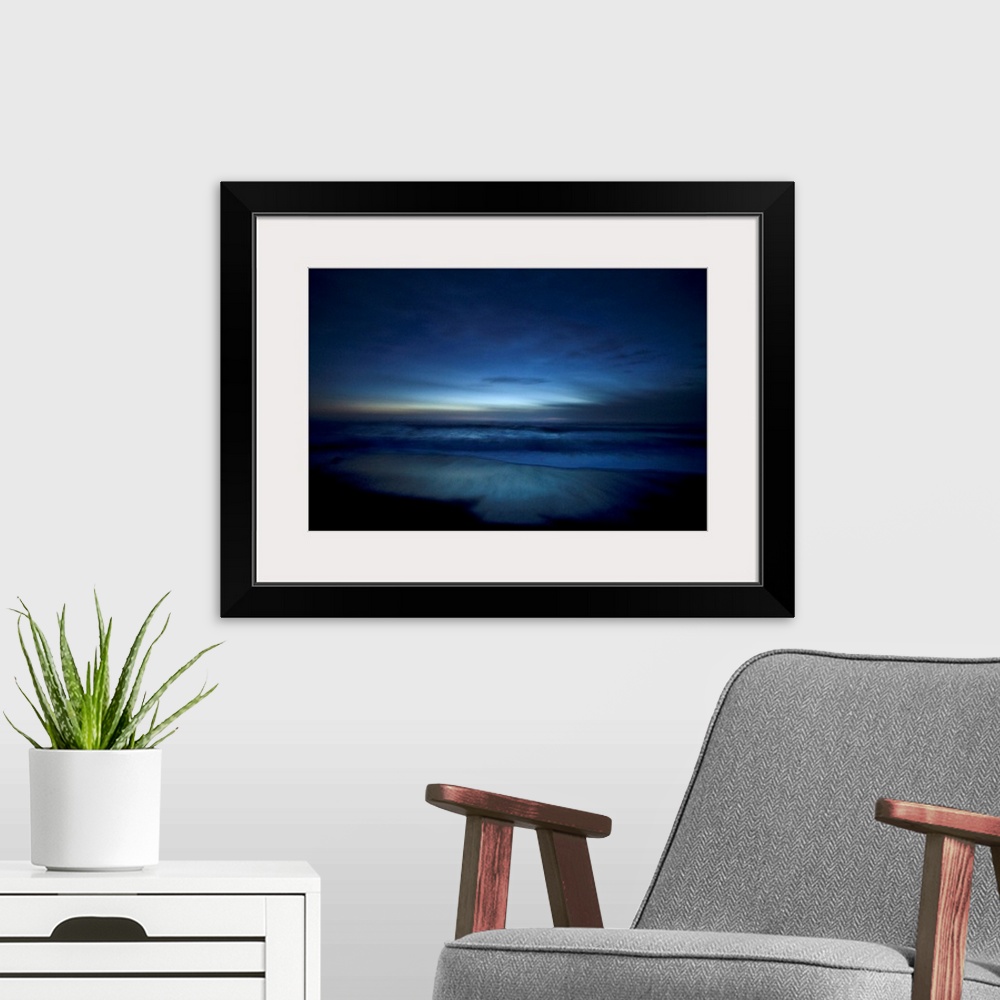 A modern room featuring Landscape, oversized photograph of deep blue ocean waters along the beach, surrounded by the dark...