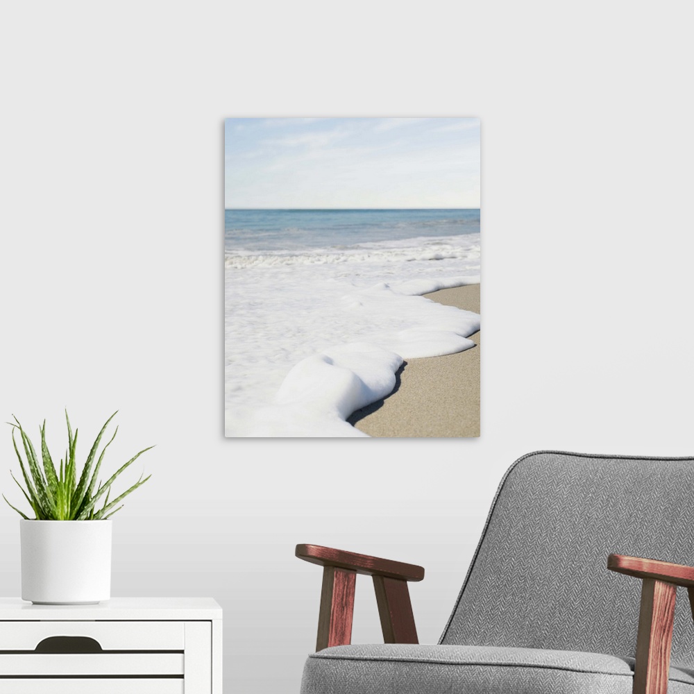 A modern room featuring Foam from a wave washing up on beach on a sunny day.