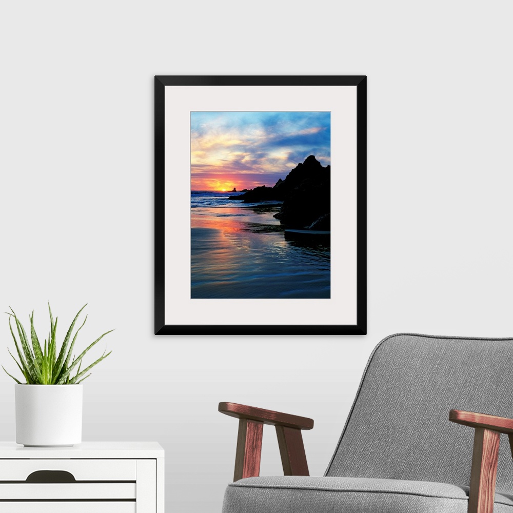 A modern room featuring Sun below the horizon in a seascape with a rocky beach and waves.