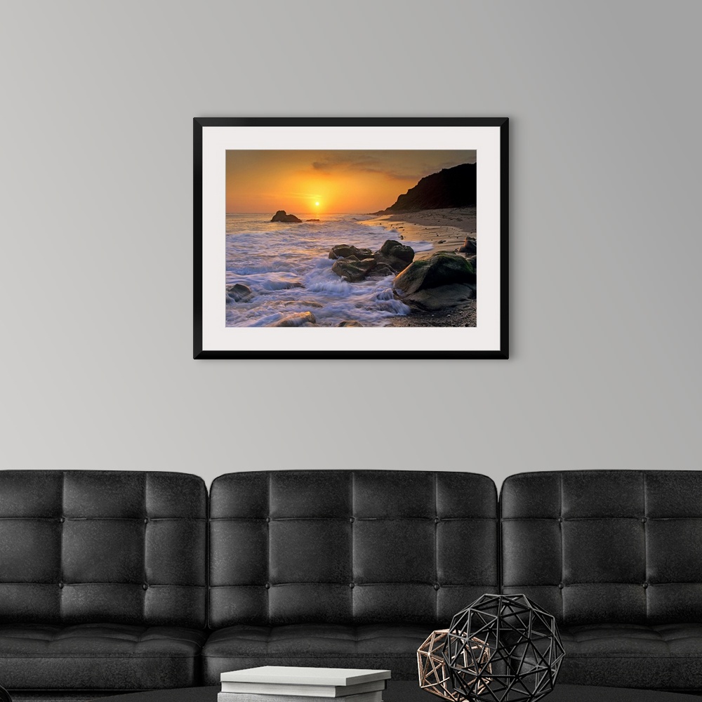 A modern room featuring Large landscape photograph of a golden sunset over the rocky shoreline at Leo Carrillo State Beac...