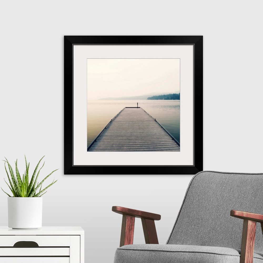 A modern room featuring Square photograph of a wooden pier leading out the the middle of a foggy lake.