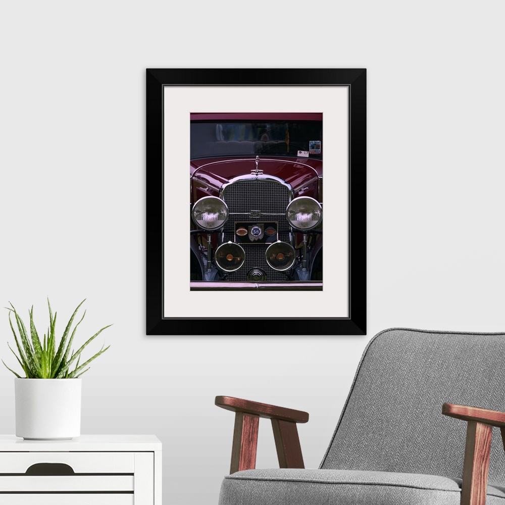 A modern room featuring The front grille and round headlights of a maroon colored vintage car.