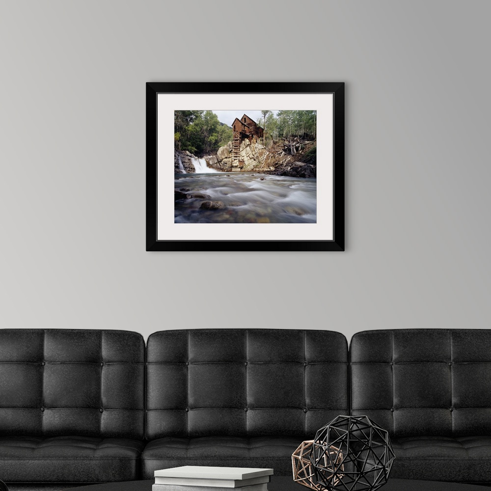 A modern room featuring Photograph of old log cabin sitting on top of rocky hill with rushing stream below.