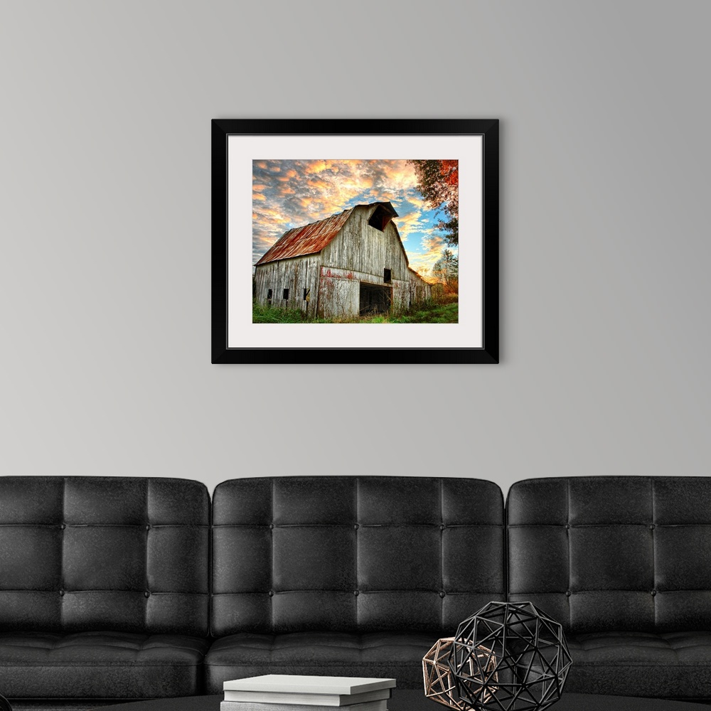 A modern room featuring Sunset over an old, weathered barn, with a cloudy sky.