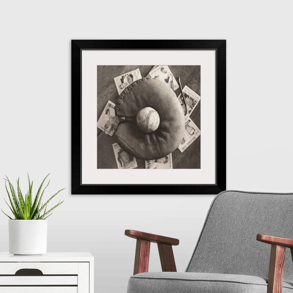 A modern room featuring Square sepia toned photograph of a worn baseball in an old mitt and vintage baseball cards behind...