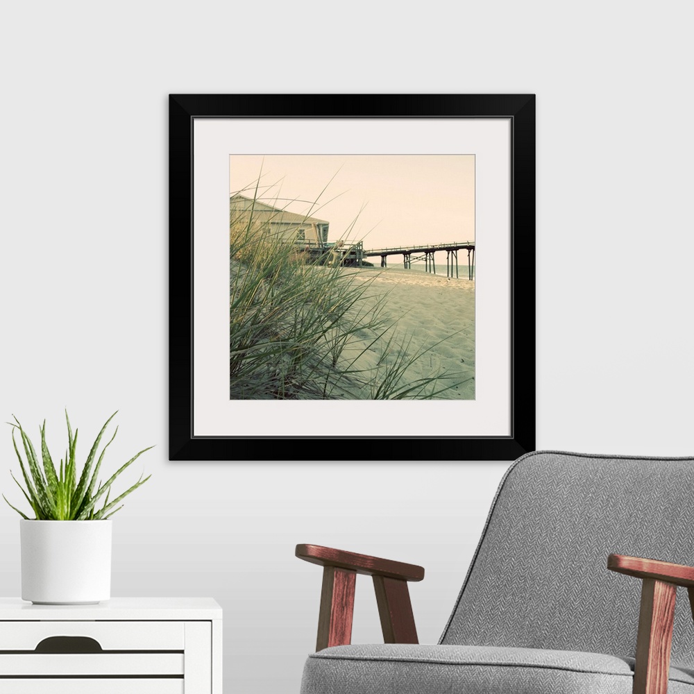 A modern room featuring Big square wall picture of grasses on a dune overlooking the beach, in the background is a buildi...