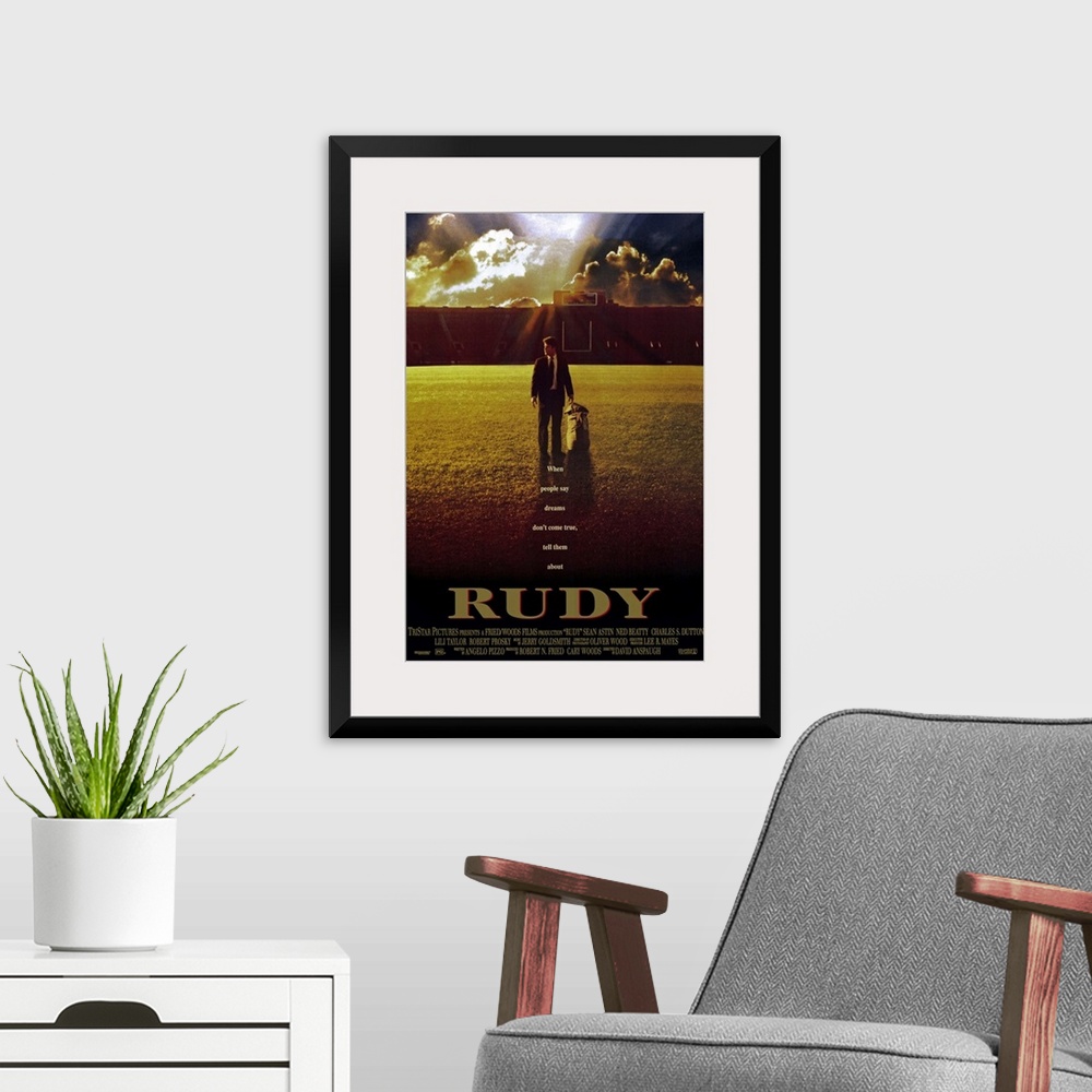 A modern room featuring This large vertical piece is a movie poster for "Rudy". It pictures the star character walking ac...