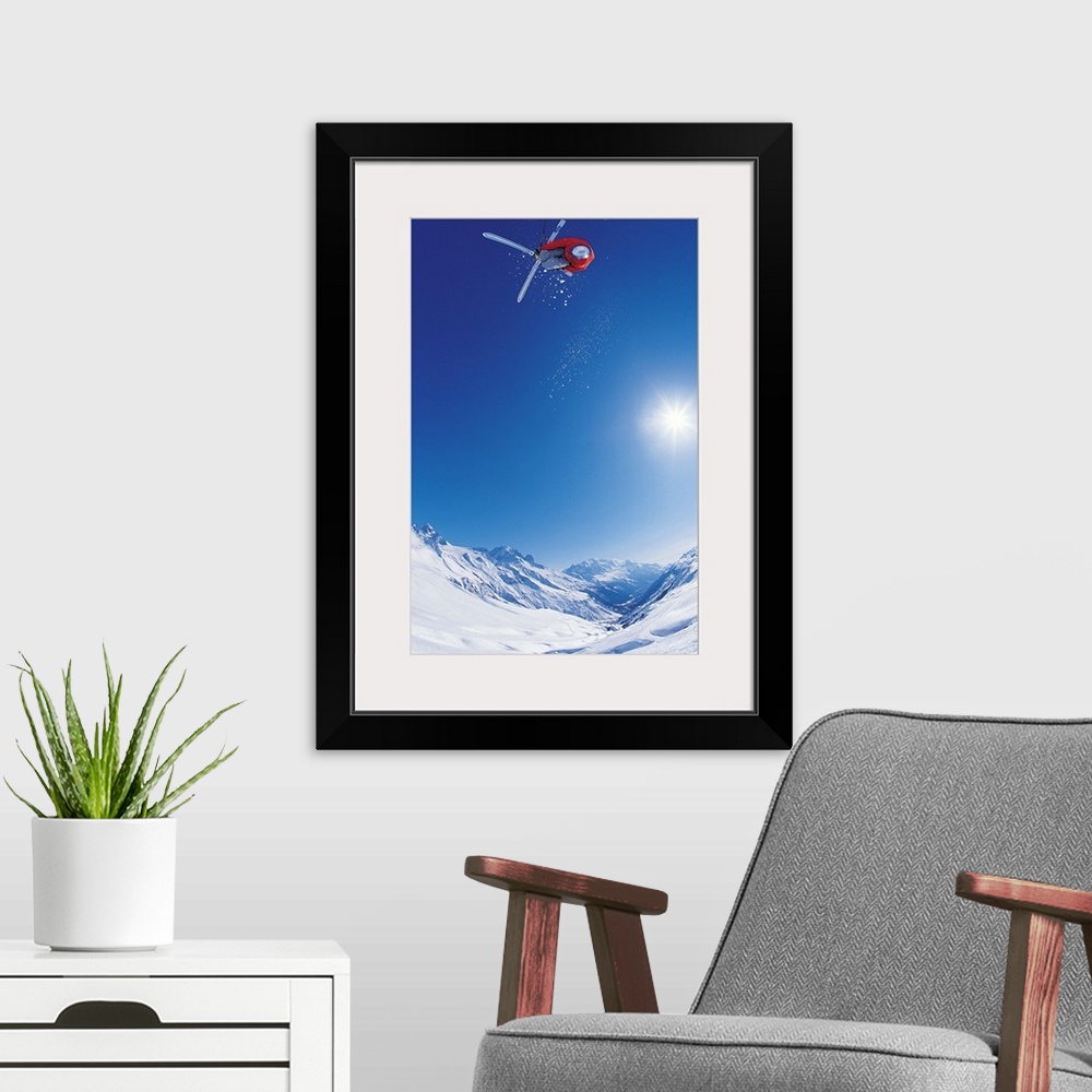 A modern room featuring Vertical photo of a man crossing his skis on as he flies through the air as the sun shines down o...