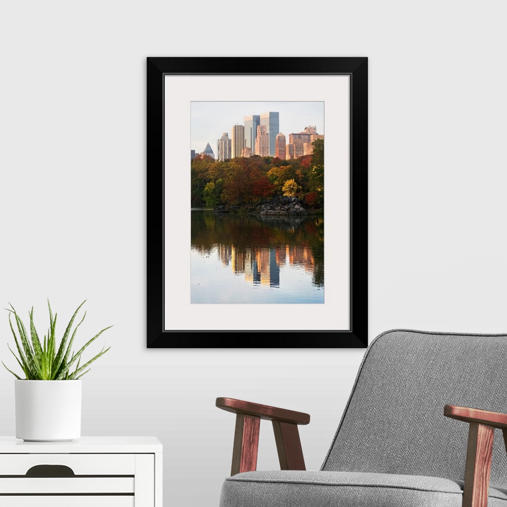 A modern room featuring This is a vertical photograph of autumn trees and skyscrapers reflecting in the calm waters of th...