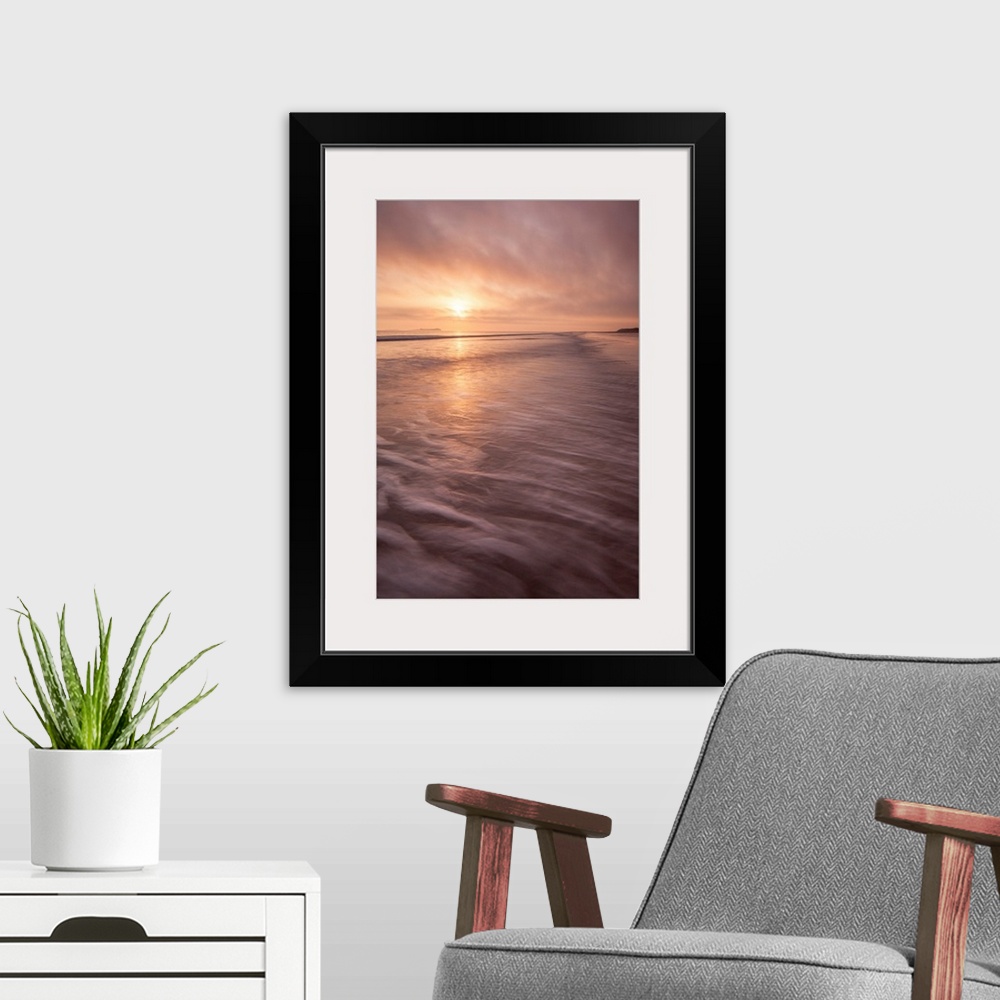 A modern room featuring A calm saescape at dawn with a glowing peach sky reflecting in the sea with swooshing waves.