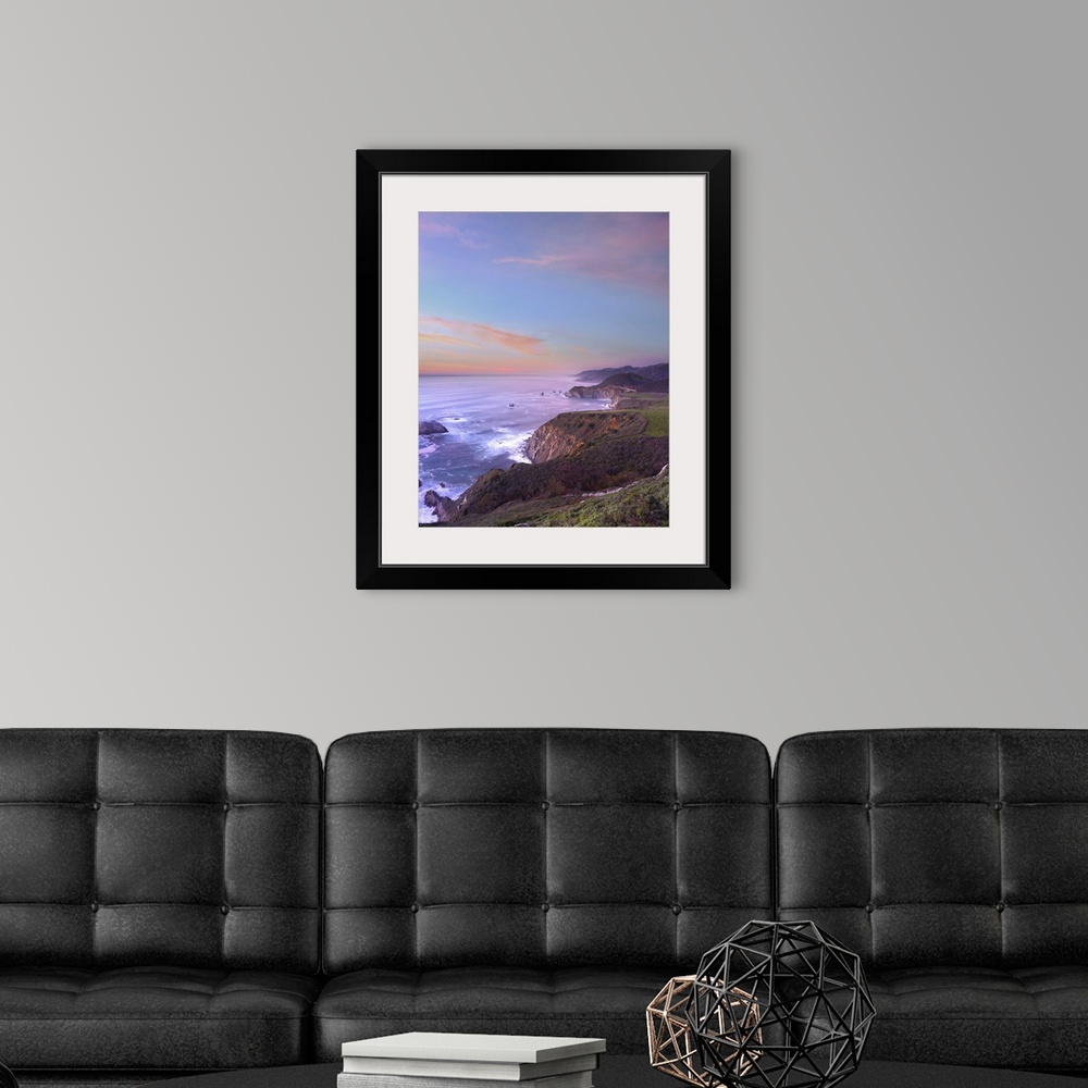 A modern room featuring Photograph of rocky cliff edge with crashing waves under a colorful cloudy sky.