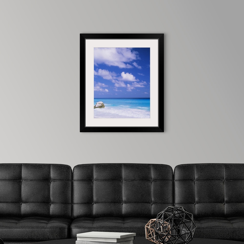 A modern room featuring Large photograph displays a lone rock sitting on a beach, while the waves of a sea begin to crash...