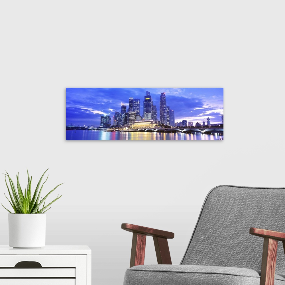 A modern room featuring A large panoramic photograph taken of a skyline in Singapore during the evening with all of the b...