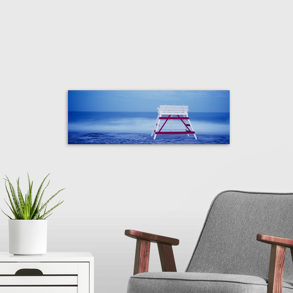 A modern room featuring Panoramic photograph on a big canvas of the back of an empty, wooden lifeguard chair sitting on t...