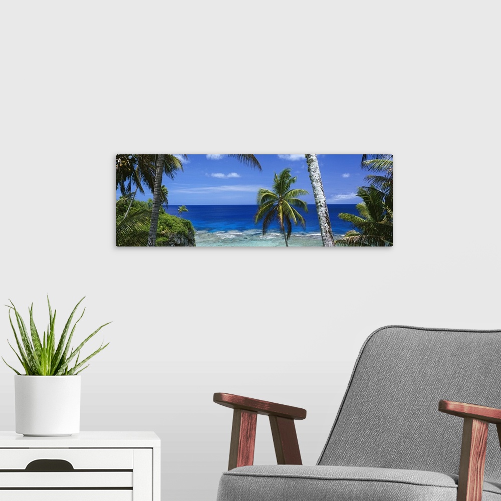 A modern room featuring Giant, panoramic photograph of palm trees on the beach of Nive Island, in front of the deep blue ...