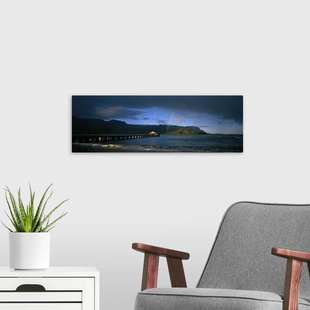A modern room featuring Picture taken of a long pier that reaches far out into the ocean with a faint rainbow shown near ...