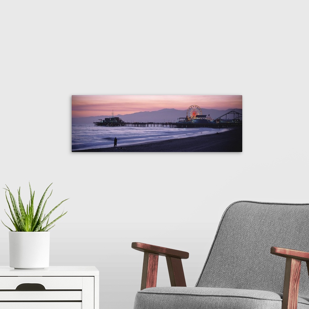 A modern room featuring A panoramic shot taken of the Santa Monica pier during sun down with a couple standing on the bea...