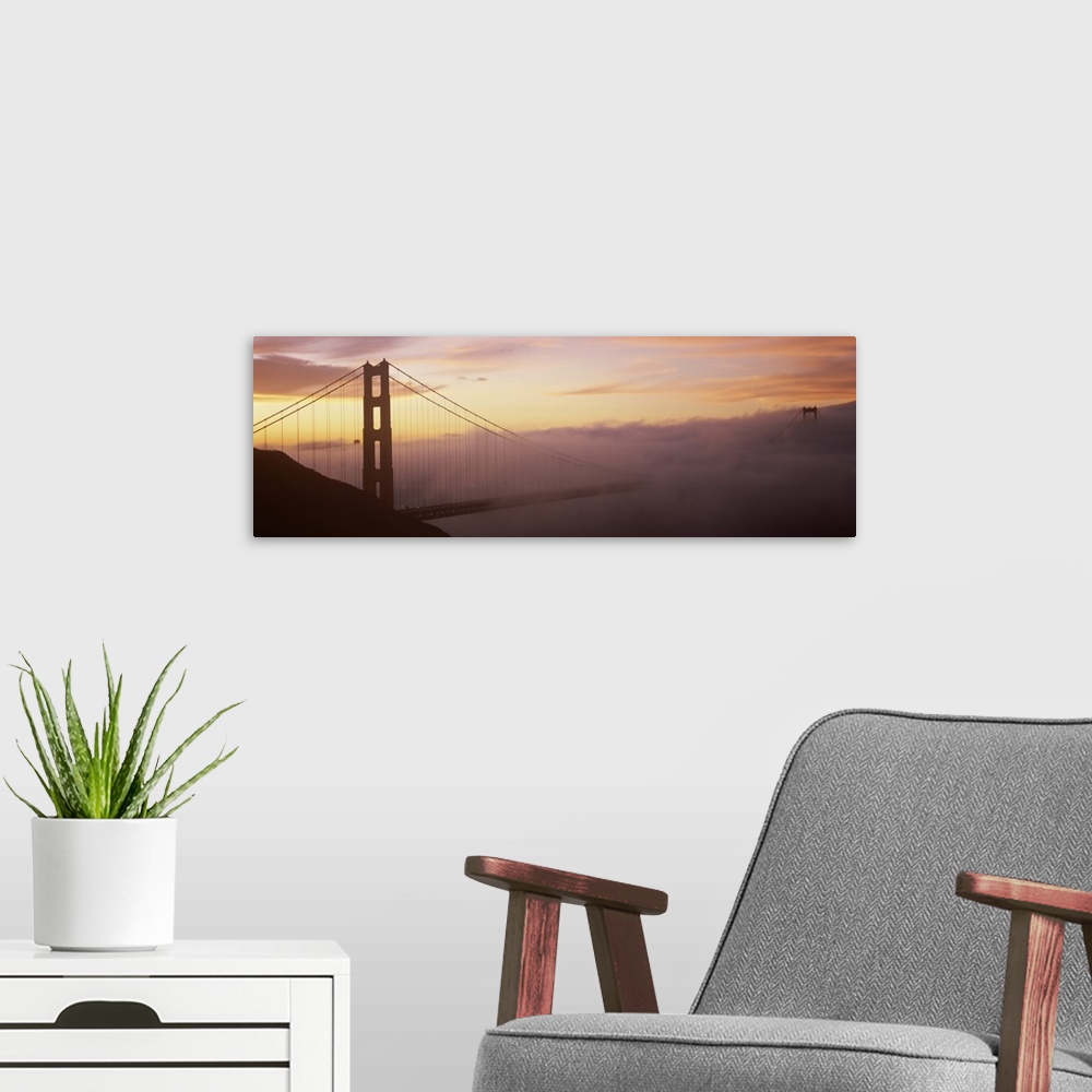 A modern room featuring Panoramic photo on canvas of the silhouette of the Golden Gate Bridge coming out of the fog at su...