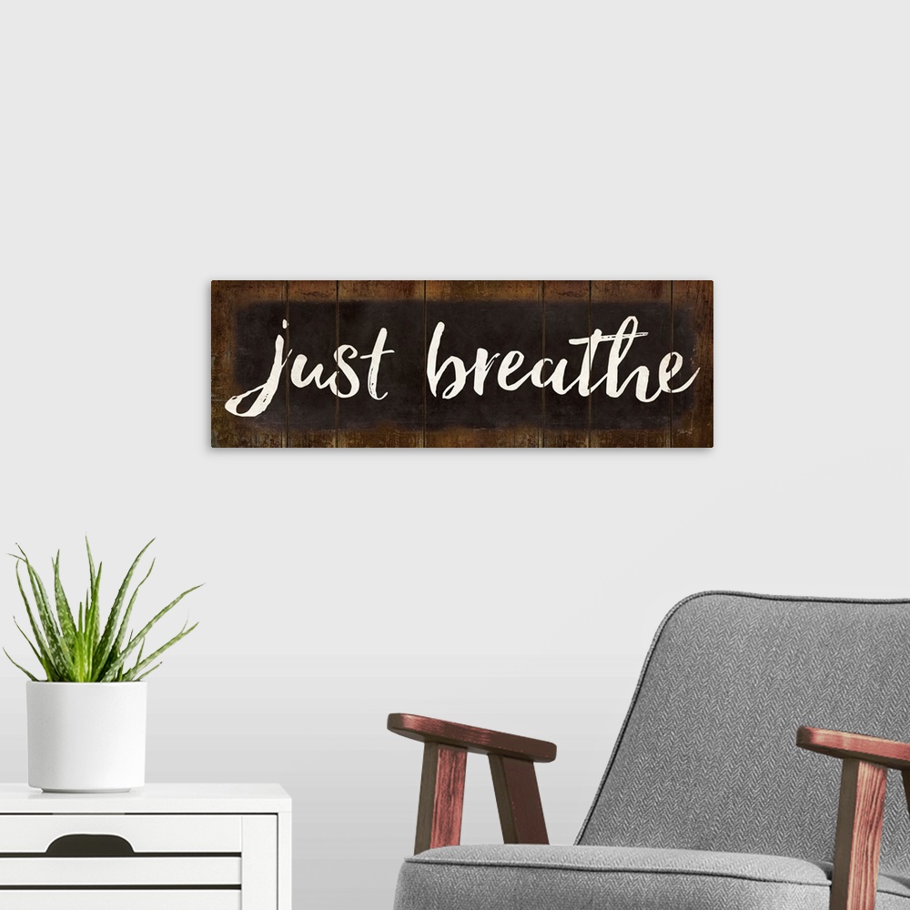 A modern room featuring "Just Breathe" in white handlettered script on a weathered brown background.