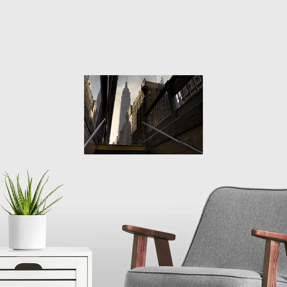 A modern room featuring Photograph looking up towards the Empire State Building in NYC from the subway staircase.