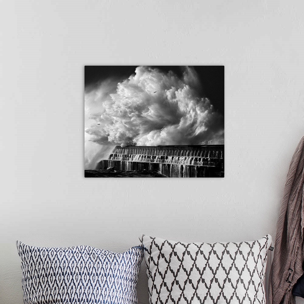 A bohemian room featuring A black and white photograph of a massive wave crashing over a pier.