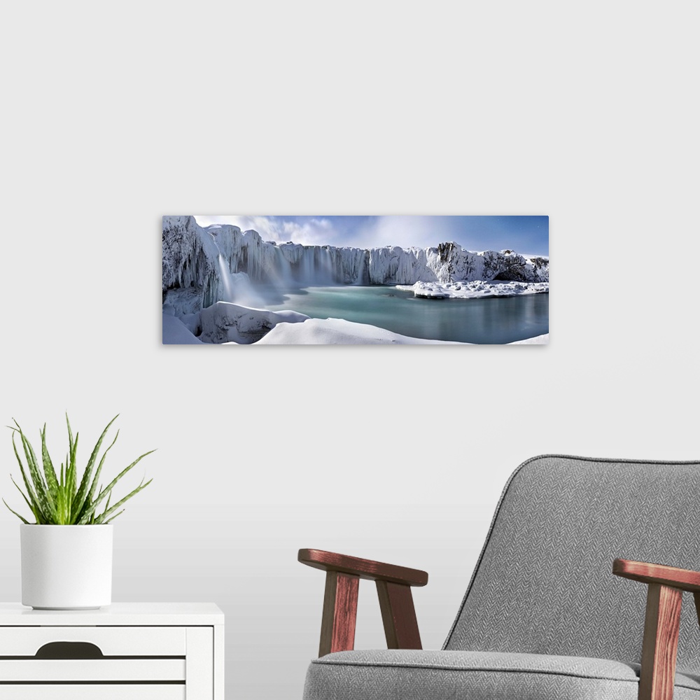 A modern room featuring Icy snow covered landscape with waterfalls streaming down from cliffs surrounding a river.
