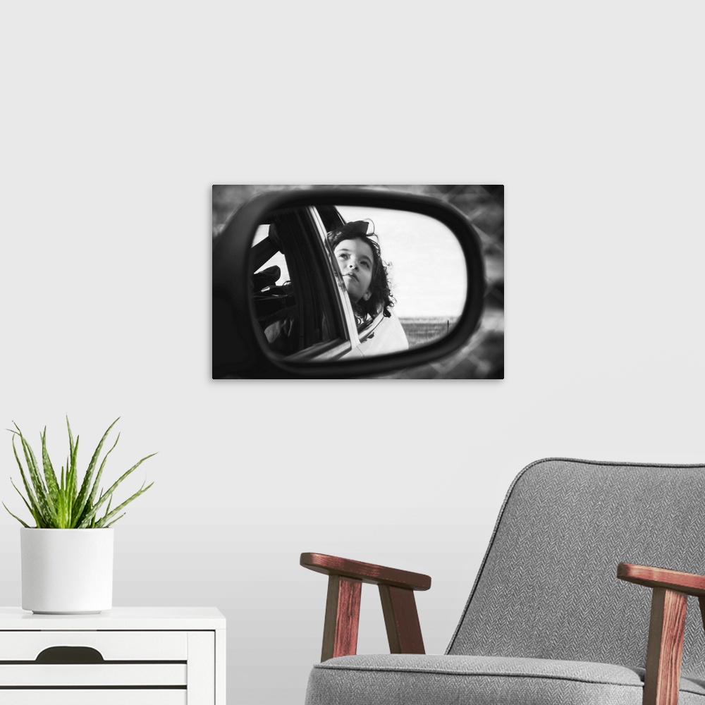 A modern room featuring Black and white photo of a young child looking out a car window, seen from a rearview mirror.