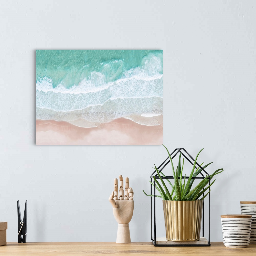 A bohemian room featuring An artistic overhead photograph of turquoise waves lapping onto a pink sandy beach. The colors in...