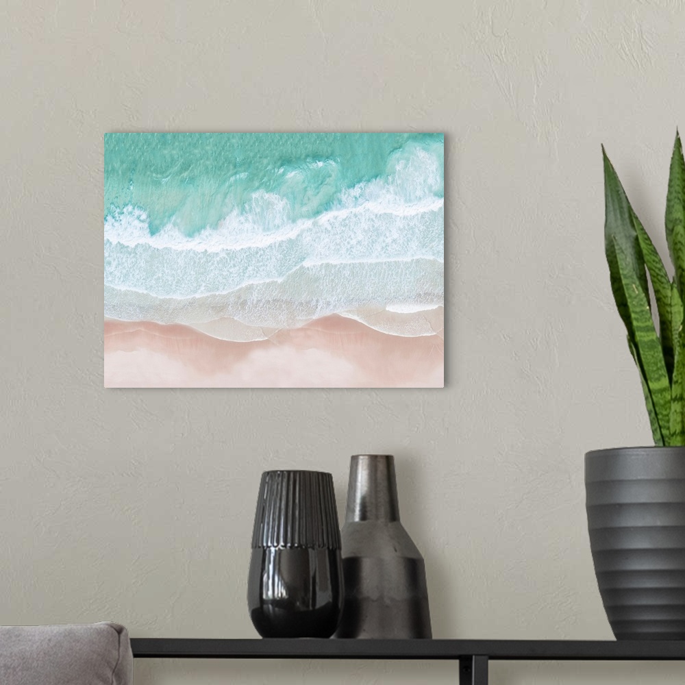 A modern room featuring An artistic overhead photograph of turquoise waves lapping onto a pink sandy beach. The colors in...