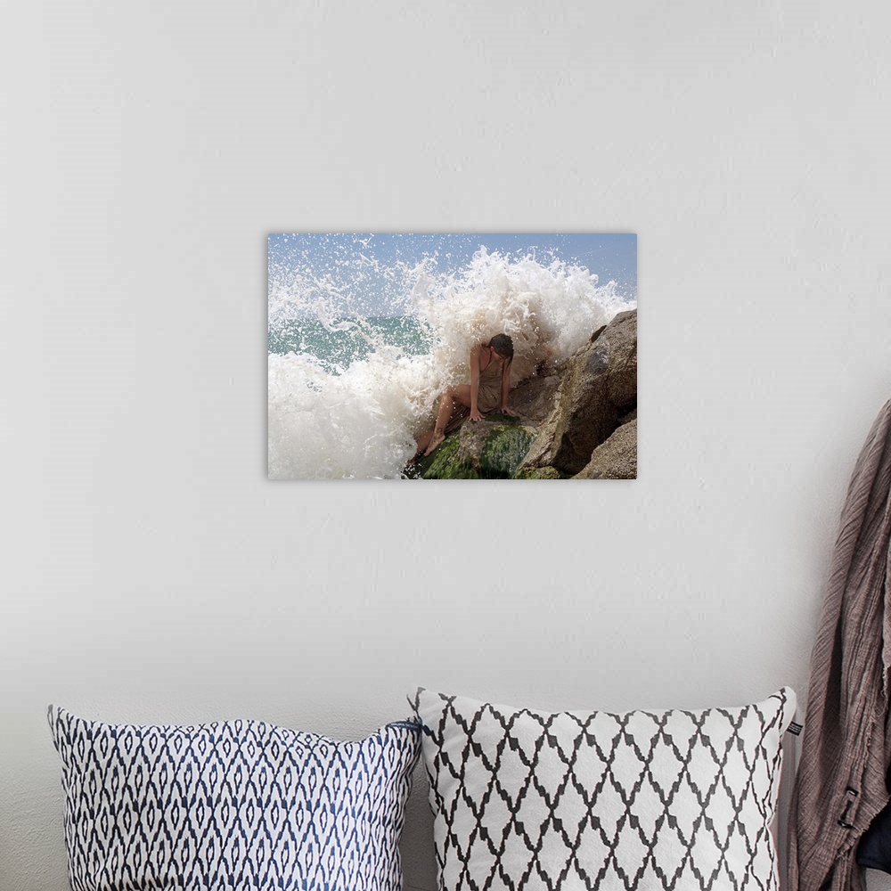 A bohemian room featuring A model on ocean rocks braces herself against the crashing waves.