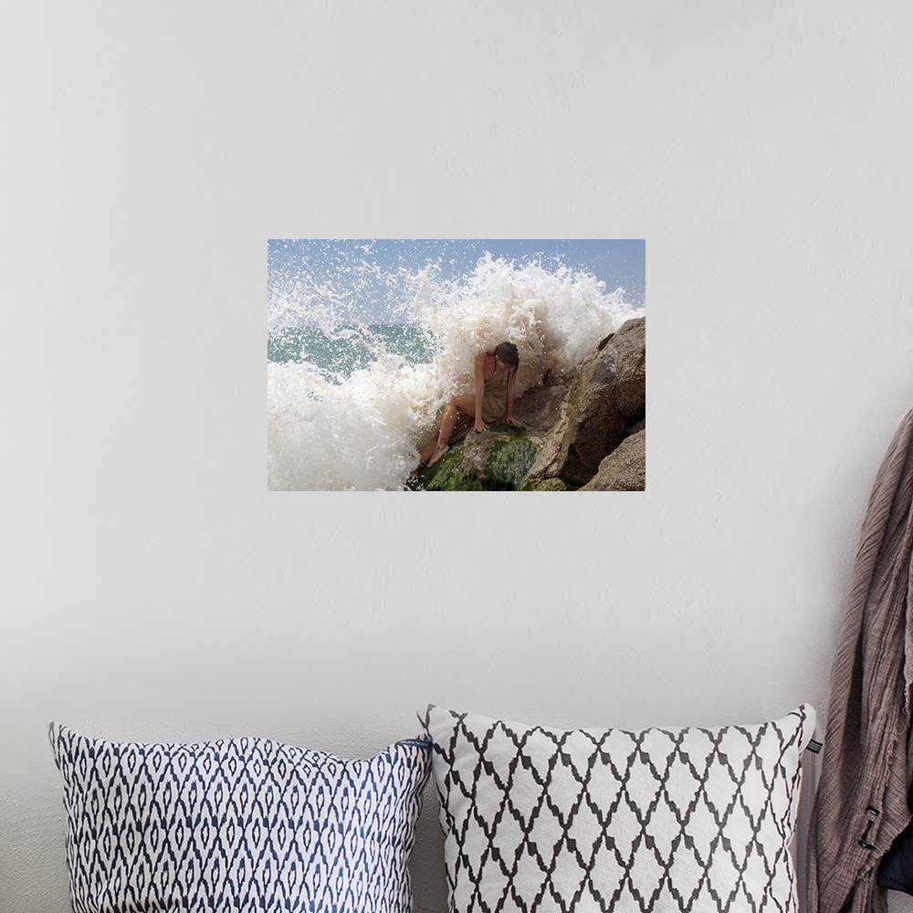 A bohemian room featuring A model on ocean rocks braces herself against the crashing waves.