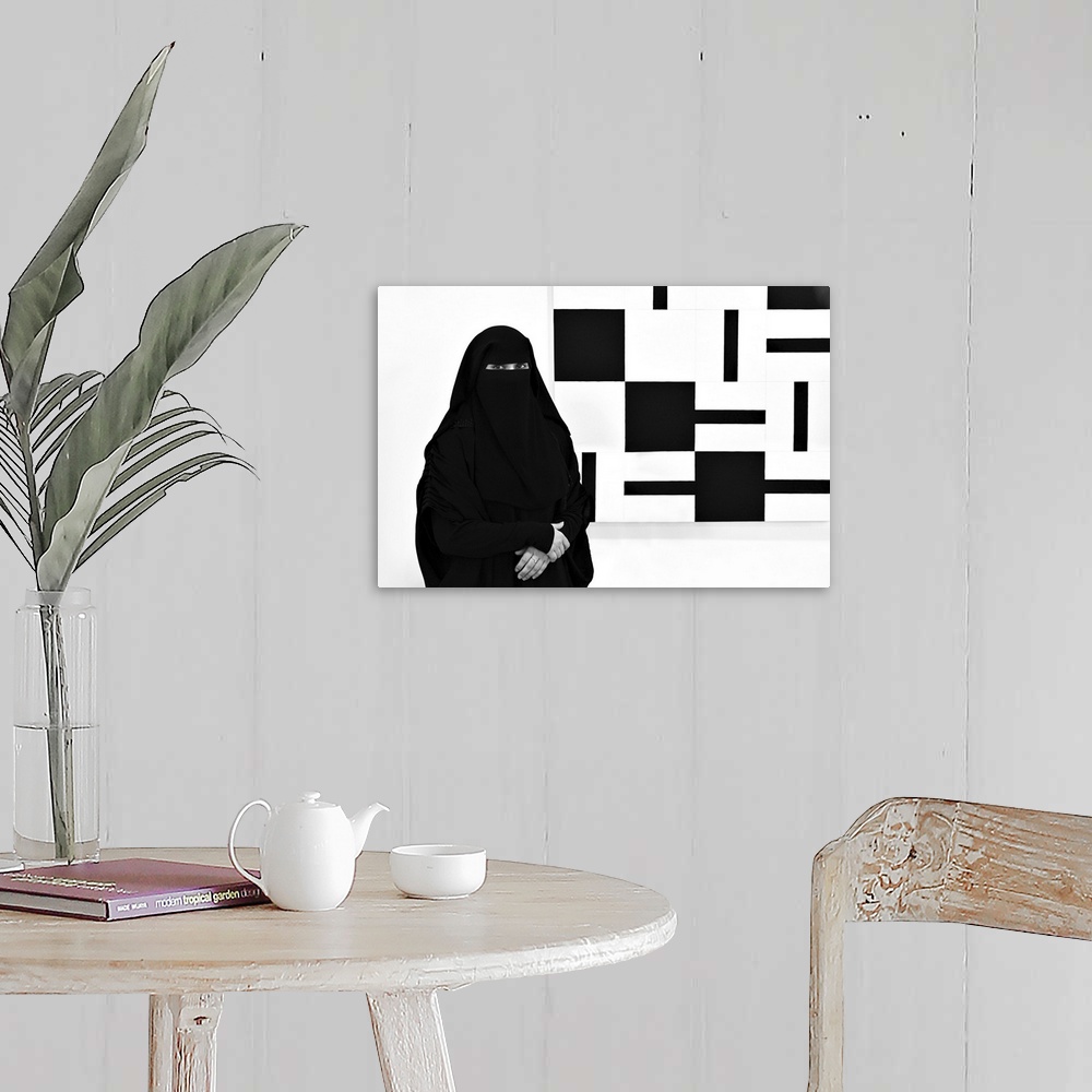 A farmhouse room featuring A woman wearing a black niqab stands next to a painting made of black and white squares.